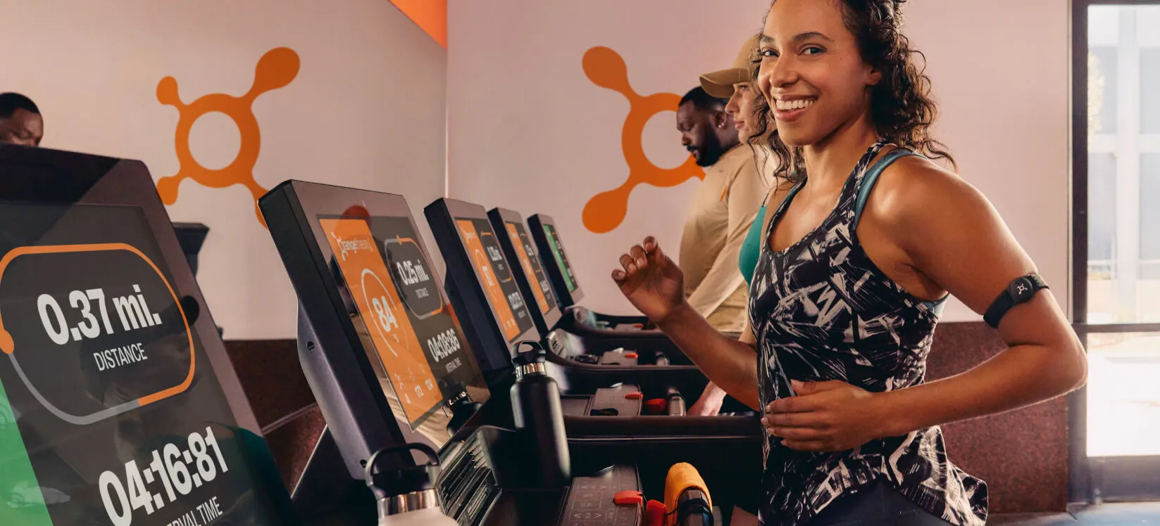 Smiling Orangetheory Fitness member running on a treadmill, tracking progress on the screen during a workout session.